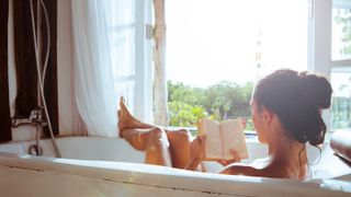 Woman relaxing in bathtub reading book - stock photo