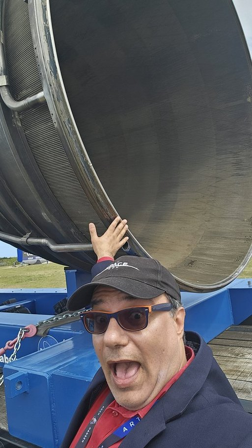 A man smiles looking at the camera while reaching back to touch a rocket engine on a plynth.
