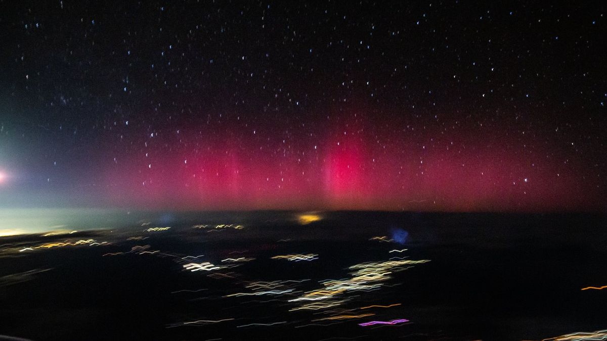 A purple aurora glows on the horizon in a picture taken from an airplane mid flight