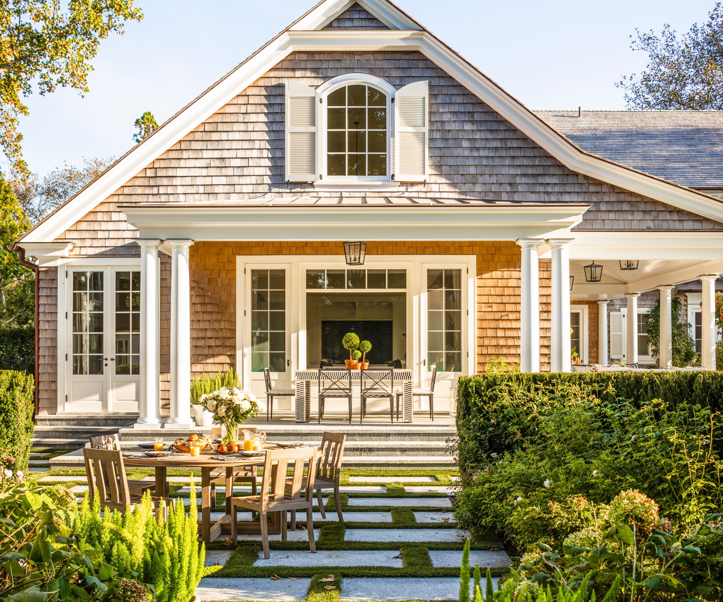 Shingle style home with large back porch and outdoor dining table and chairs