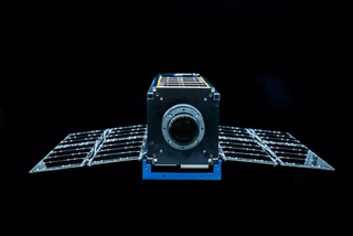 Moonlighter satellite, a small cube-shaped craft with solar panel wings on either side, against a black background.