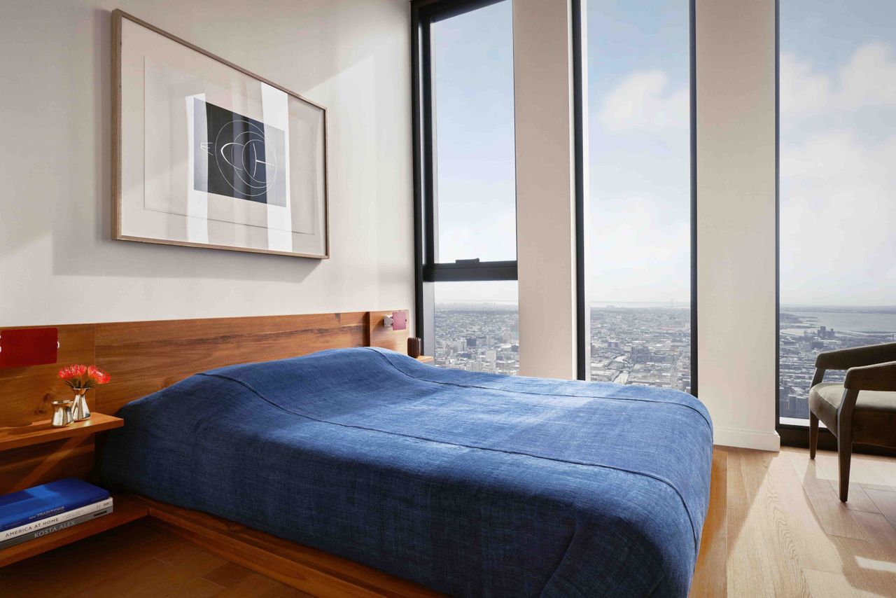 Apartment with bed with dark blue bedding on wooden floor with floor to ceiling windows and a stunning view