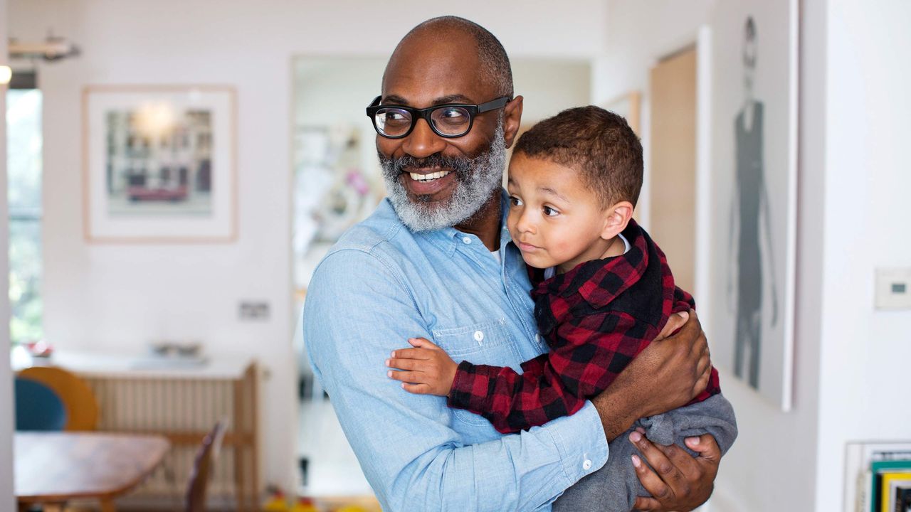 A smiling grandpa holds his toddler grandson.