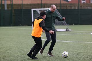 Prince William playing soccer with a boy wearing an orange vest