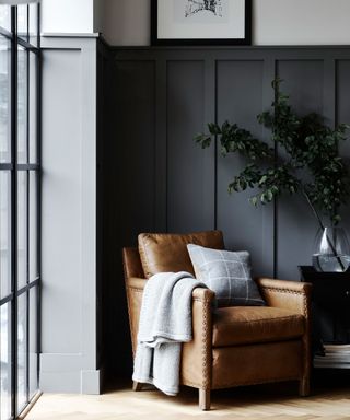 Corner of living room, gray paneled walls, white upper walls, brown leather armchair with cream throw and cushion