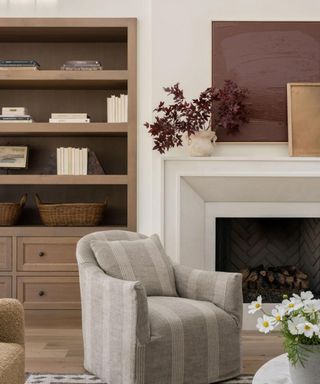 neutral living room with rust colored art and dark red faux foliage in a vase on the mantel