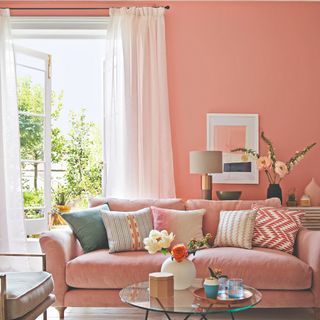 A peach-painted living room with a matching velvet sofa with voile curtains