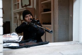 Jin Ha as Marshall, aiming a sniper rifle out the window as he sits in a pre-war apartment, in 'Only Murders in the Building.'