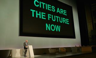 Lord Foster giving a keynote speech, with a slide stating "CITIES ARE THE FUTURE NOW"