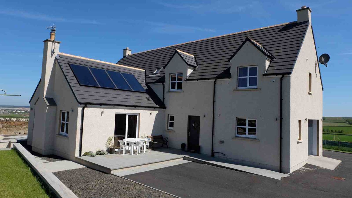 A two-storey, white-rendered house in Scotland. The new build has a traditional feel with dormer windows in the roofline, and also features a single-storey wing to one side.