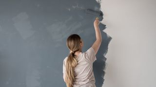 The three colours you should avoid using in your bedroom if you want a restful night's sleep - woman painting her room dark grey