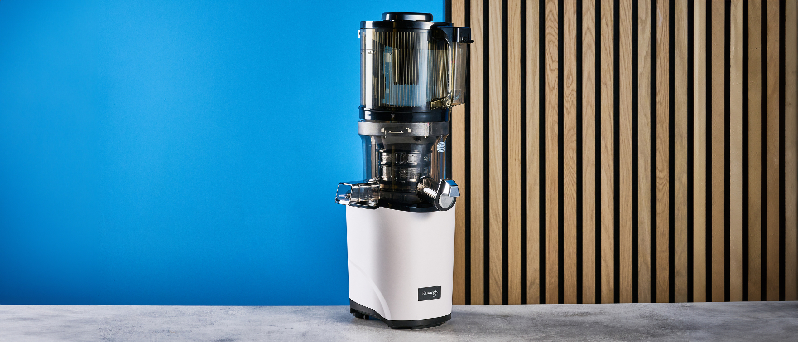 Kuvings Auto8 hands-free slow juicer photographed on a blue background.