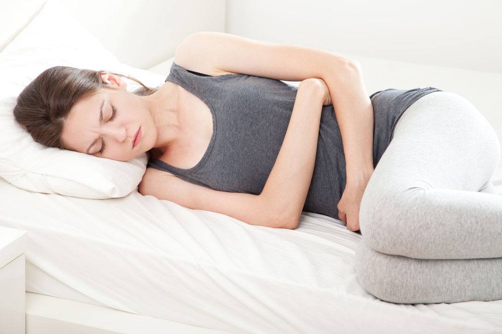 A woman lays in bed clutching her stomach