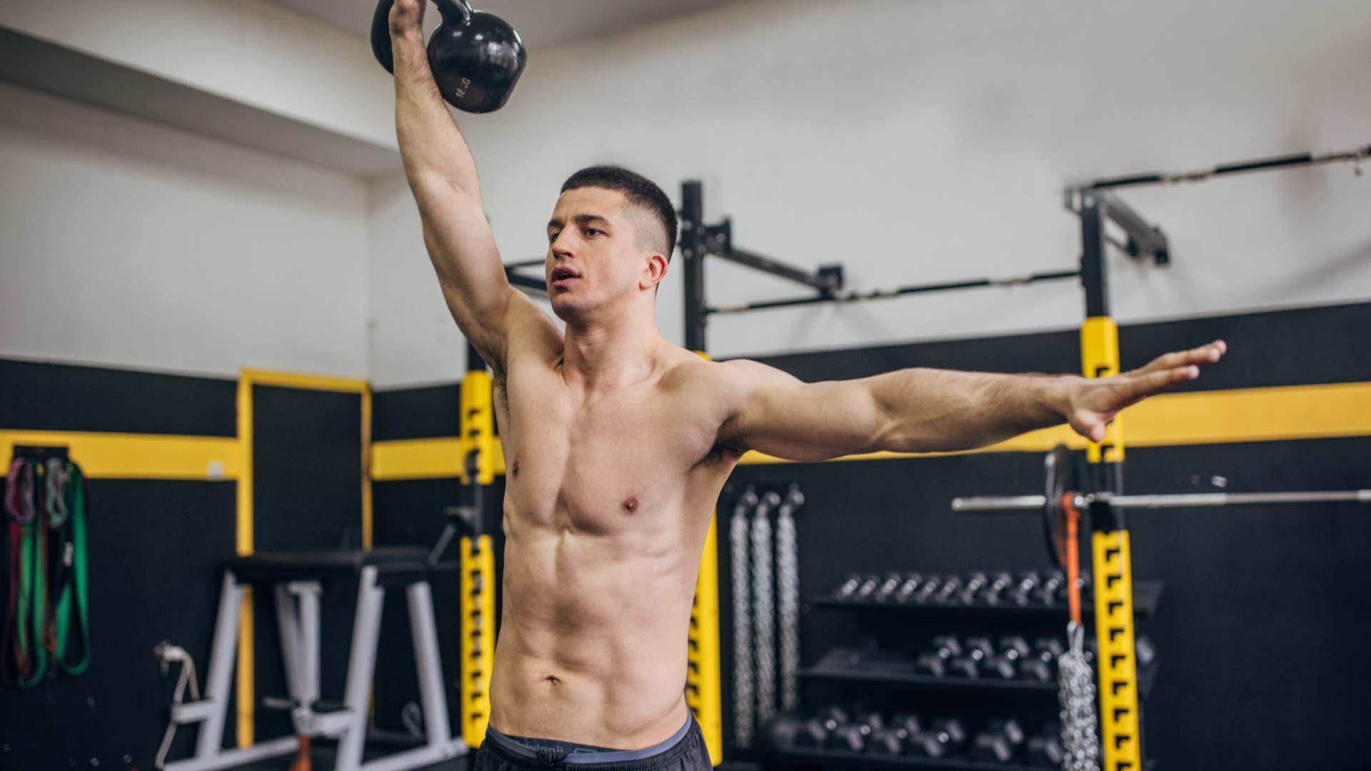 A man performing a standing core exercise, the overhead kettlebell march