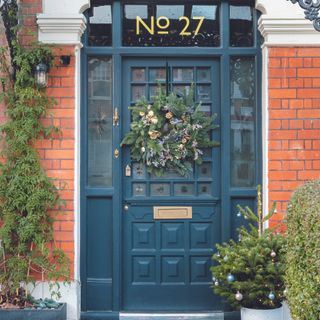 Navy front door with classic Christmas wreath and mini trees.