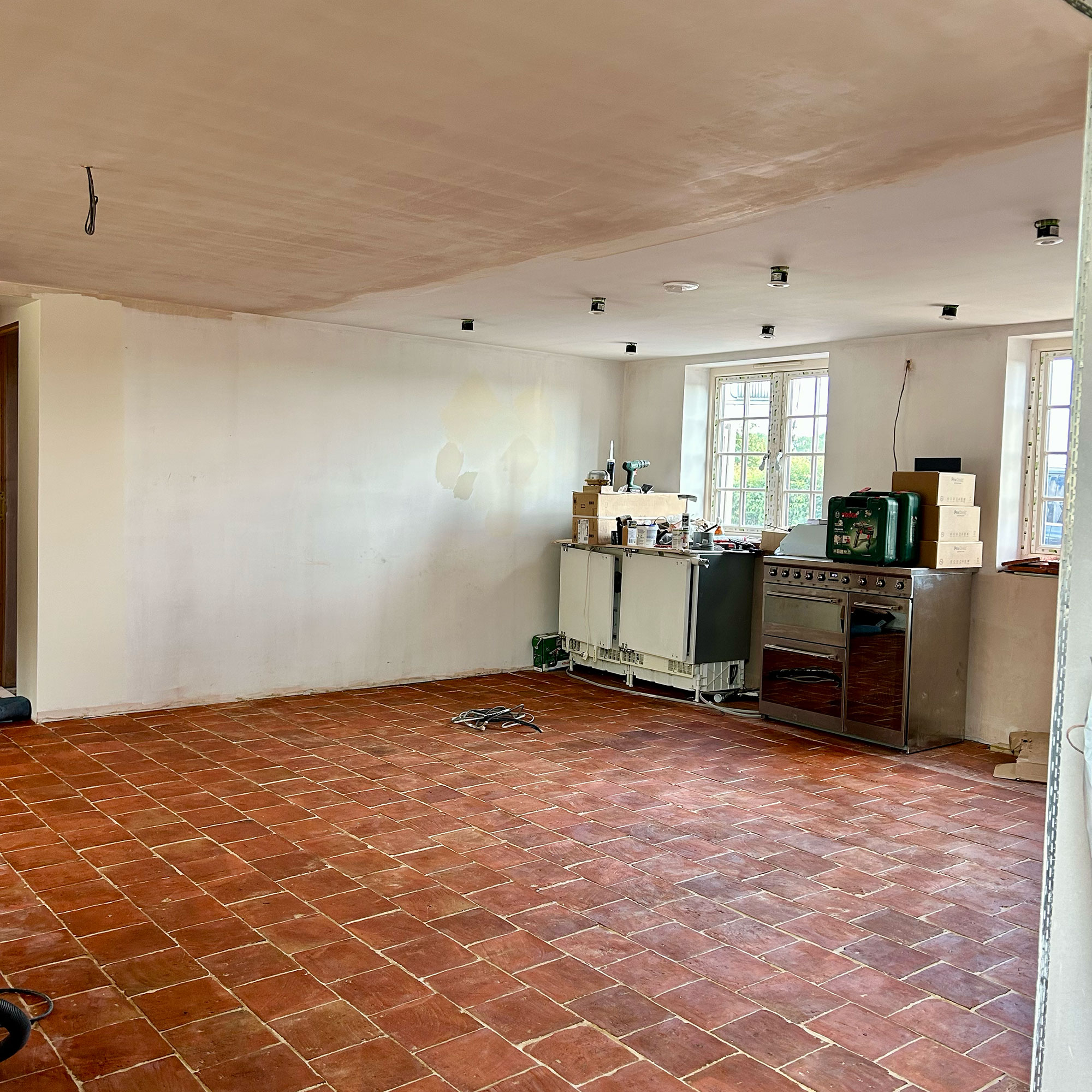 Kitchen mid-renovation with terracotta tiles floors, a few appliances against wall and exposed wiring