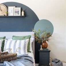 Bedroom with painted accent wall, blue toned bedding and decorative cushions, bedside table with flowers in vase