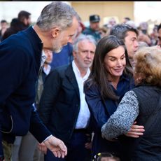 Queen Letizia hugging a woman as King Felipe looks on in a crowd of people