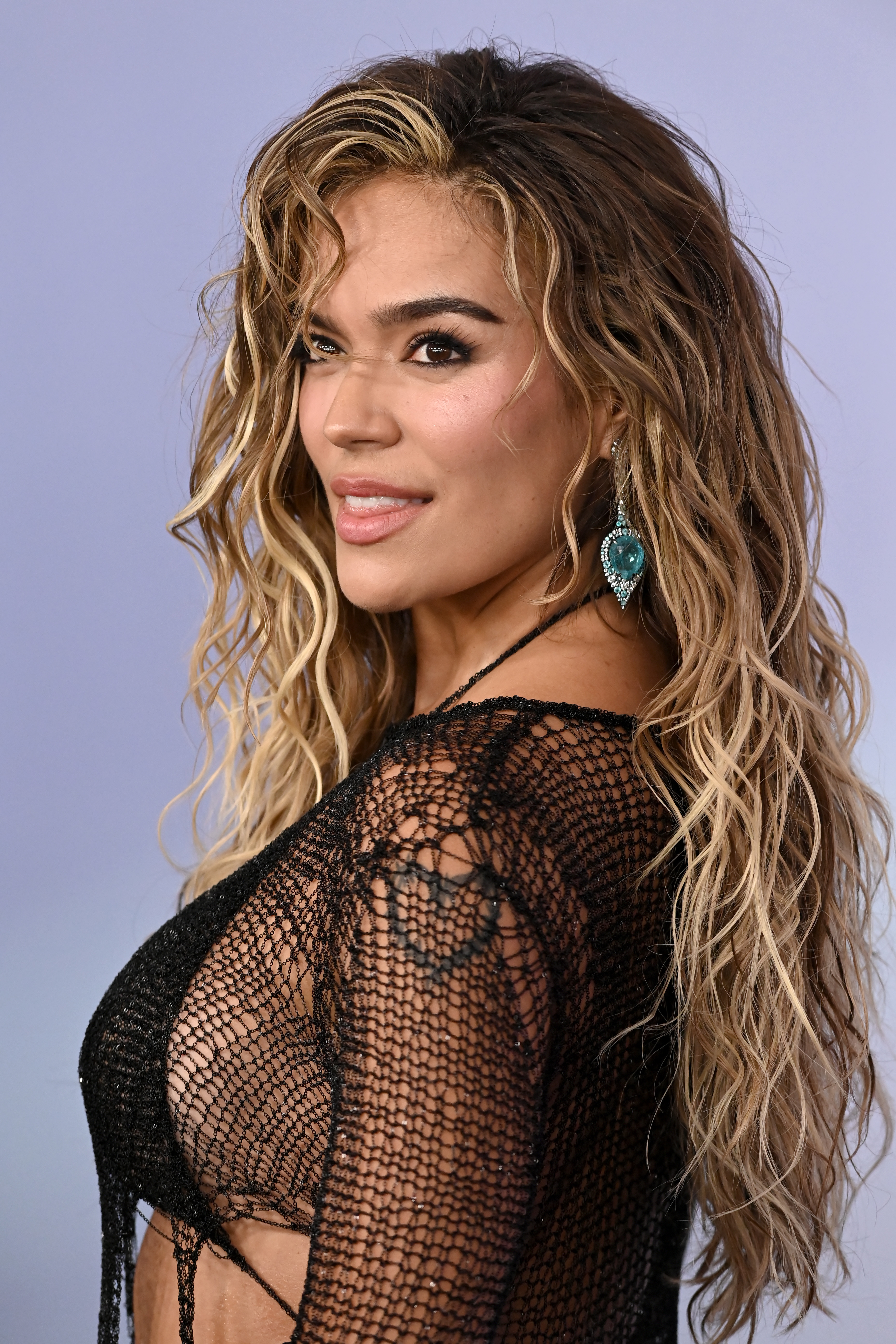a latina woman with long, honey blonde hair poses for paparazzi during a red carpet event