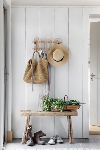 white hallway with shiplap walls, rustic bench and rail, baskets and hat, grey stone floor
