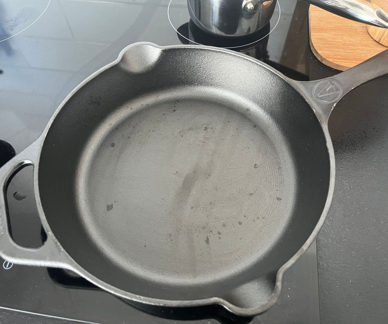A small black cast-iron skillet on a black stove with water droplets inside