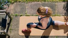 Woman doing lunges as part of a bodyweight exercises routine at home, standing on yoga mat in sunny garden