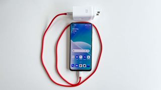 The OnePlus Nord 2T with its 80W charger and red USB-C cable wrapped around it