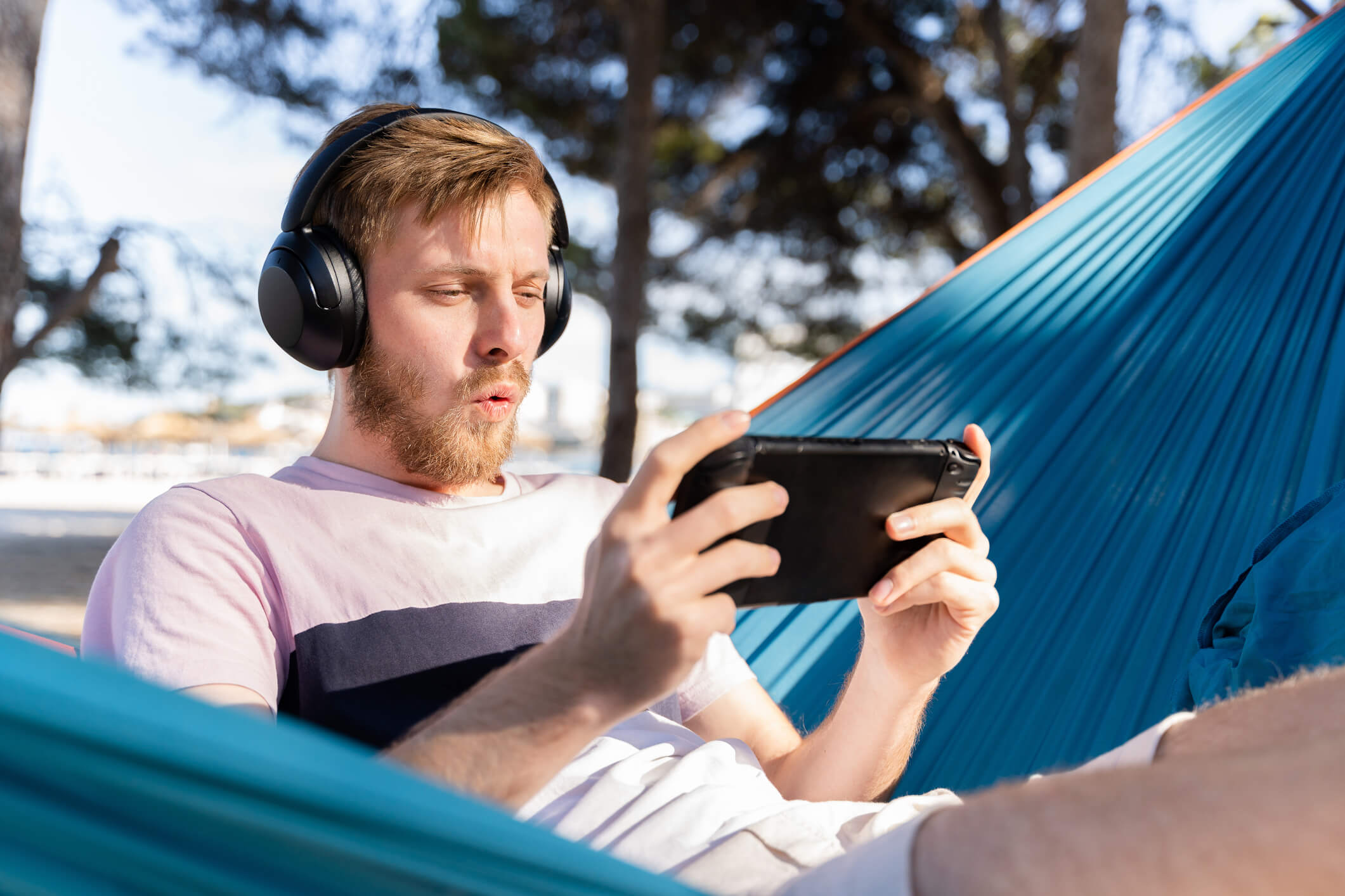 Someone sat down playing a handheld gaming console while wearing headphones