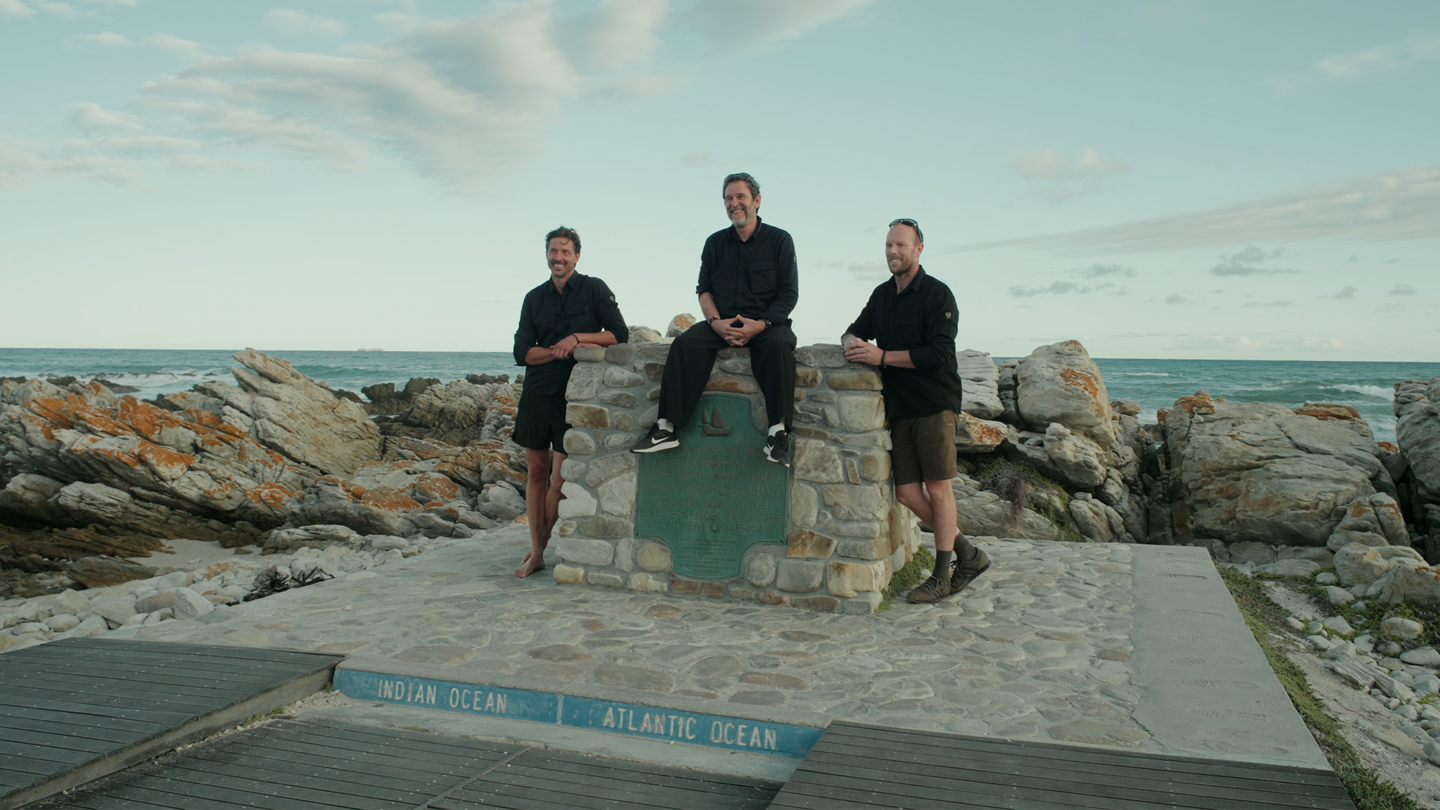 Three men stood at a stone wall with a plaque on it.