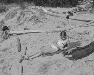 A black and white photo of a young girl lounging on the sand