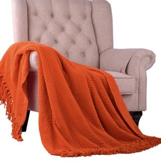 A burnt orange throw on a beige upholstered chair