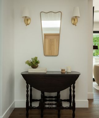neutral entryway with an antique table and wavy mirror with wall sconces