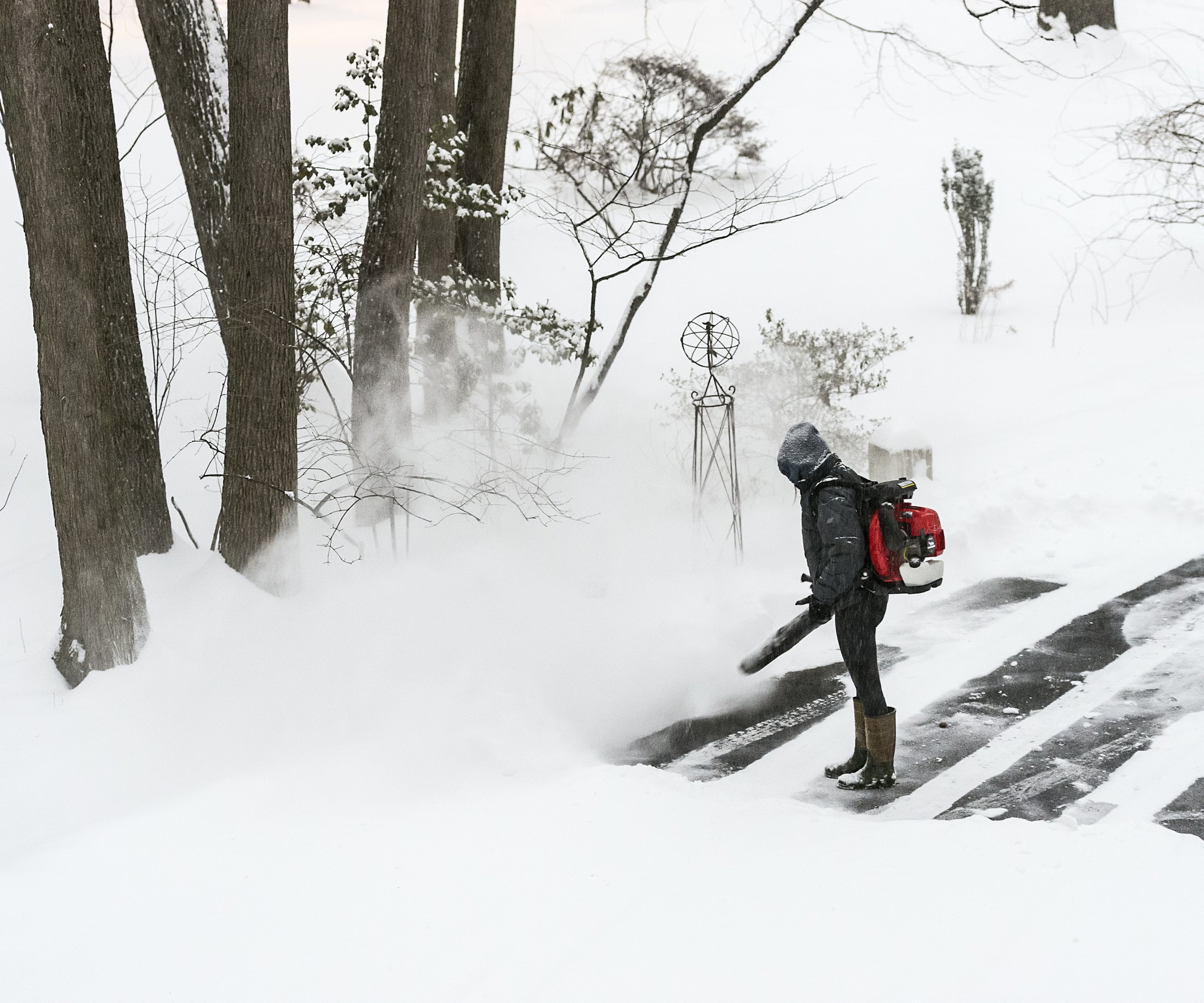 A person is clearing thick snow off their driveway with a snow blower