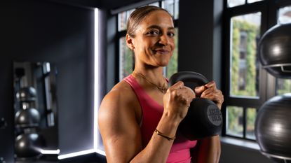 Trainer Joslyn Thompson Rule smiles at the camera in a sports top holding a kettlebell in her hands.