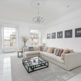 living room with white wall cream colour sofa with designed cushions frames on wall and windows