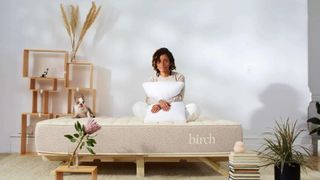Woman sits on Birch Natural Talalay Latex Mattress surrounded by springtime flowers