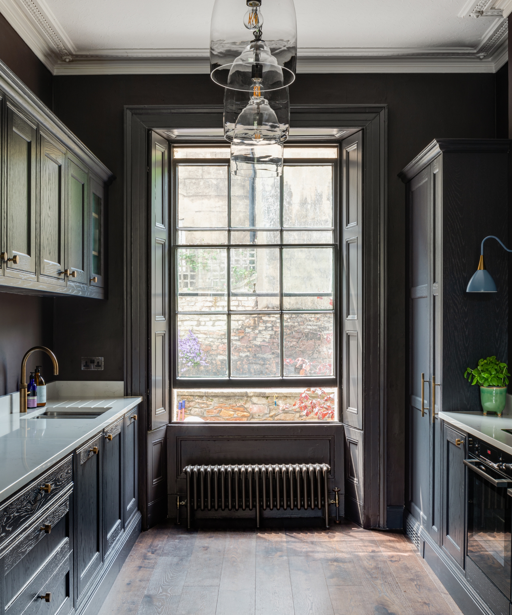 a galley kitchen with warm charcoal cabinets and a slightly more brown-toned wall color. At the end of the galley is a large sash window letting in plenty of light