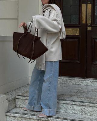 London woman wears light wash baggy jeans with a cream scarf jacket and mesh flats.