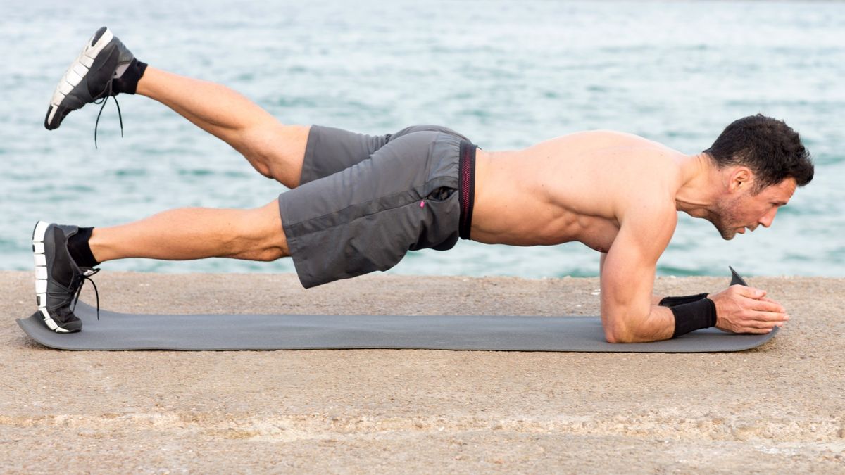 Man performing a one-leg forearm plank outdoors