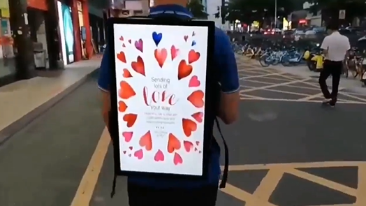 A 21.5-inch digital signage display showing hearts on someone&#039;s back as they walk through a convention.