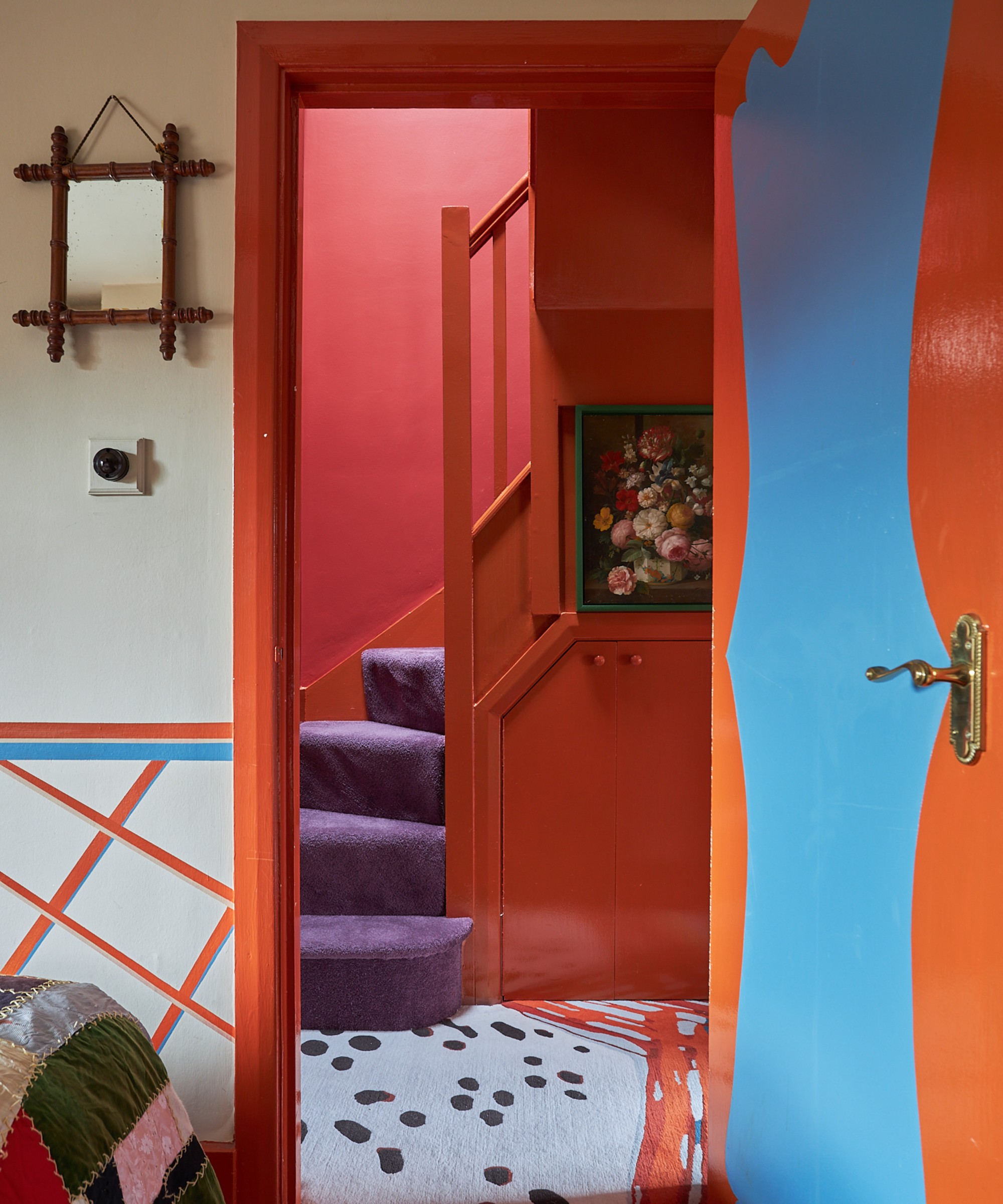 A bring orange hallway painted in Farrow &amp;amp; Ball&#039;s Charlotte&#039;s Locks with a purple runner on the staircase
