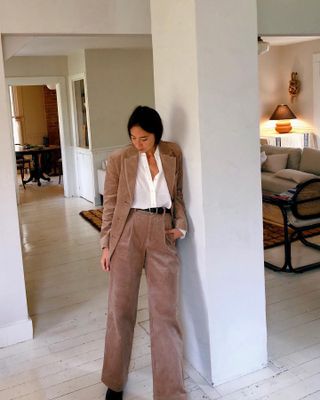 A woman wears a brown corduroy blazer, a white button-down shirt, a black belt, and corduroy trousers.