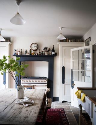 Cream kitchen with a classic cream stove, navy blue painted fireplace and rustic wooden dining table.