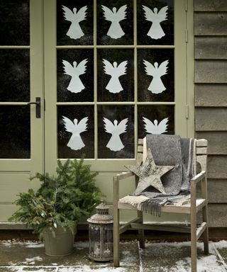 Christmas porch decor ideas with a seat, grey blanket and white angels in the windows of a set of French doors