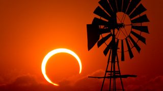 A bright orange sunset sky shows the 2012 annular eclipse with the shadow of a windmill.
