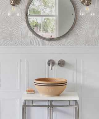 white small bathroom with patterned basin, white textured wallpaper, mirror, pair of wall sconces
