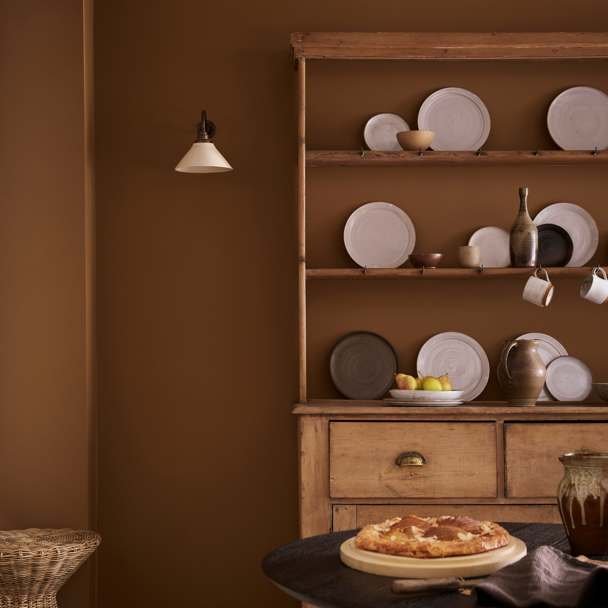 a brown wall of a kitchen with wooden dresser and wall light