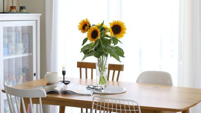 unflowers in a glass vase with a cup of coffee, candle, eyeglasses, and magazine on the table