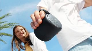 Anker Soundcore Mini 3 held in a hand on blue sky background