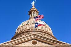 Dome of Texas State Capitol building with the U.S. flag and Texas flag waving in the foreground